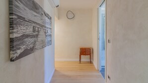 Un pasillo con piso de madera, un cuadro en la pared izquierda, una pequeña mesa de madera y una puerta al final.