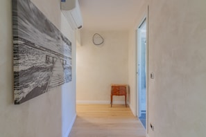 Ein Korridor mit Holzboden, einem Gemälde an der linken Wand, einem kleinen Holztisch und einer Tür am Ende.