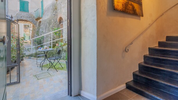 Una escalera que conduce a un segundo piso, una puerta a un espacio exterior con una mesa y sillas, y un cuadro en la pared.