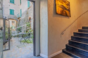 A staircase leading to a second floor, a door to an outdoor area with a table and chairs, and a painting on the wall.