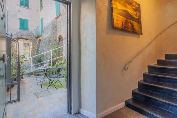 Eine Treppe führt zu einer zweiten Etage, eine Tür zu einem Außenbereich mit Tisch und Stühlen, und ein Gemälde an der Wand.