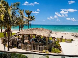 Ein Restaurant direkt am Strand mit einem Reetdach, Sitzgelegenheiten im Freien und Meerblick.