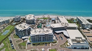 Ein Luftbild eines Küstenhotelkomplexes mit mehreren Gebäuden, einem zentralen Poolbereich und einem Strand.
