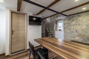 A kitchen with a wooden table, a black chair, a stone wall, and a TV mounted above the counter. - Casa di Pietra Apartment (Split)