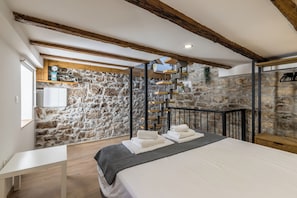 A bedroom with a stone wall, wooden beams, a bed with towels, a white table, and a hanging rack. - Casa di Pietra Apartment (Split)