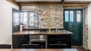 A kitchen with a stone wall, wooden beams, a sink, and a green door. - Casa di Pietra Apartment (Split)