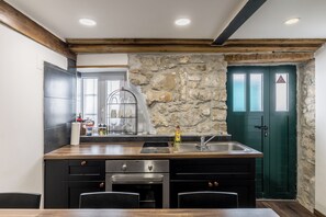 A kitchen with a stone wall, wooden beams, a sink, and a green door. - Casa di Pietra Apartment (Split)