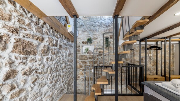 A room with a stone wall, a staircase, a bed, and a small plant. - Casa di Pietra Apartment (Split)