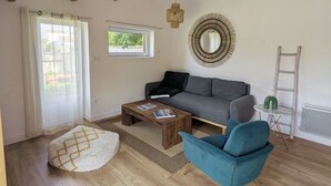 Een woonkamer met een bank, een salontafel, een blauwe fauteuil, een houten plafond, een raam en een spiegel aan de muur.