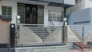 Una entrada con reja y una escalera que conduce a un edificio con ventanas protegidas por barrotes y una puerta.
