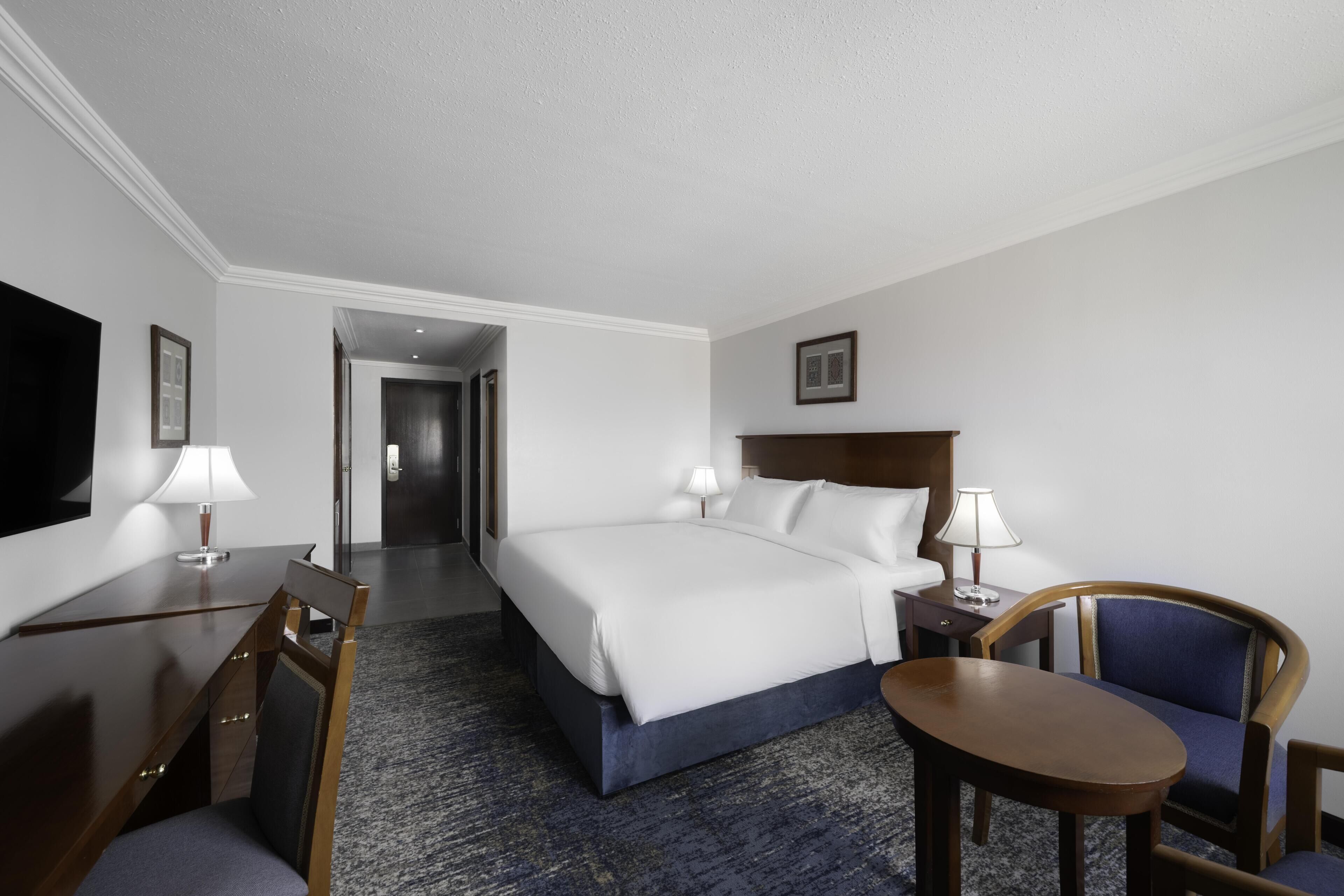 A hotel room with a bed, desk, chair, and a TV.