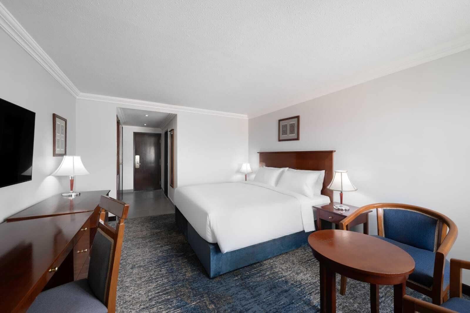 A hotel room with a bed, desk, chair, and a television.