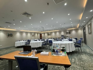 A conference room with round tables, chairs, and a projector. - Al Mubarakia Hotel Yanbu (Yanbu Al Bahr)