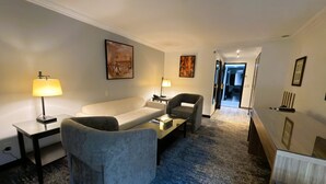 A hotel room with a sofa, armchair, and a desk with a lamp. There are paintings on the walls and a carpeted floor. - Al Mubarakia Hotel Yanbu (Yanbu)