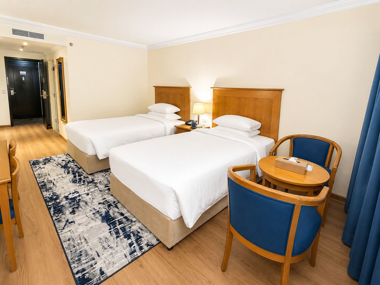 A hotel room with two beds, a desk, a chair, and a small table.