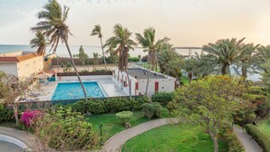 A pool area with a view of the sea, surrounded by palm trees and greenery. - Al Mubarakia Hotel Yanbu (Yanbu)