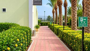 A pathway lined with palm trees and yellow flowers, leading to a building labeled 'Health Club.' - Al Mubarakia Hotel Yanbu (Yanbu)