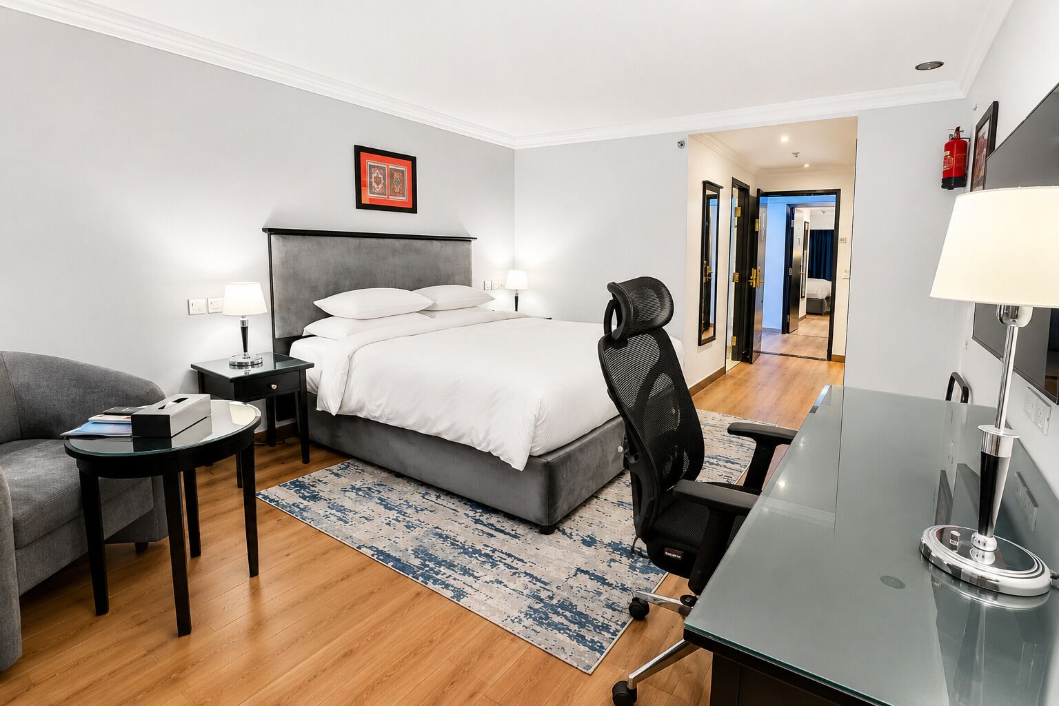 A hotel room with a bed, a desk, a chair, a sofa, and a rug.