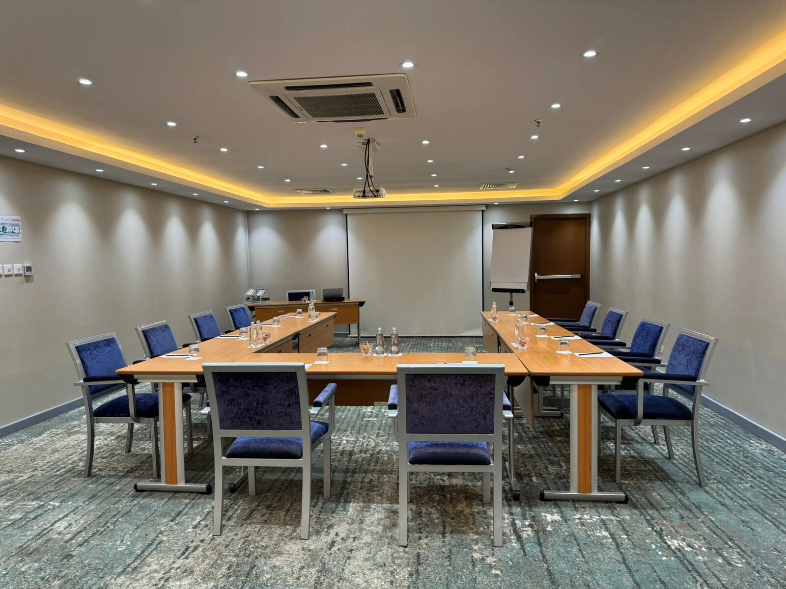 Un salón de conferencias con una mesa larga, sillas azules y piso alfombrado.
