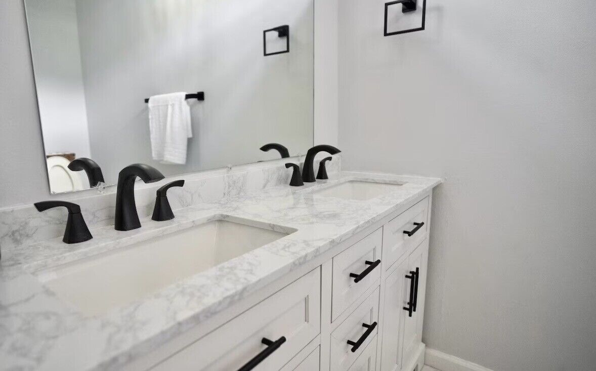 A bathroom with two sinks, a large mirror, and white cabinets with black handles.