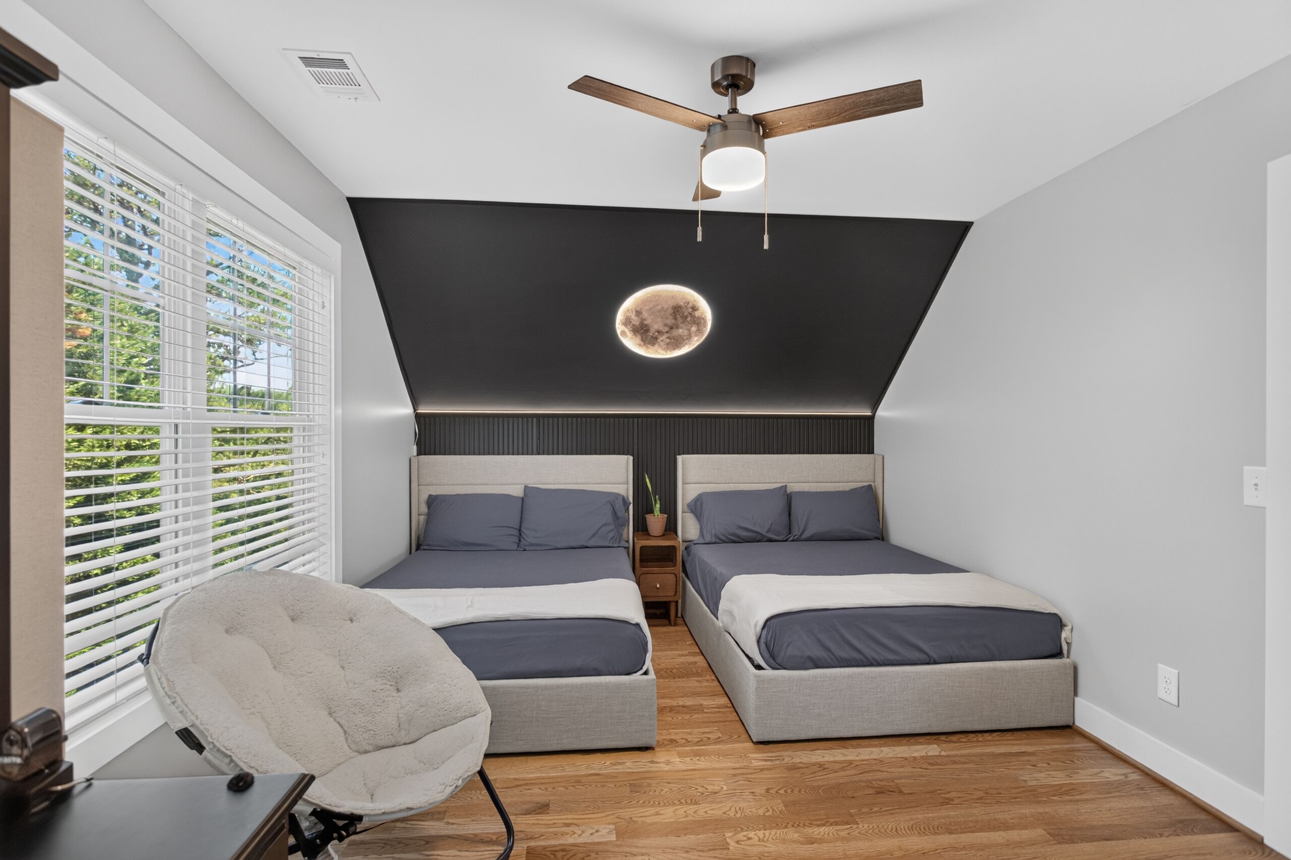 A bedroom with two beds, a ceiling fan, a wall-mounted light, and a window with blinds.