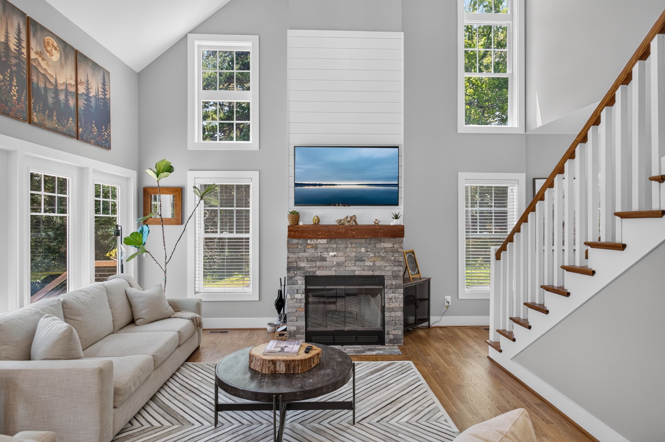 A spacious living room with a fireplace, large windows, and a staircase.