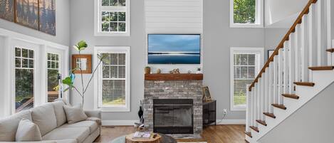 A spacious living room with a fireplace, large windows, and a staircase.
