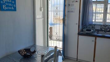 Eine kleine Küchenzeile mit Spüle, ein Fenster mit Vorhang, eine Tür mit Schild und ein Tisch mit kariertem Tischläufer.
