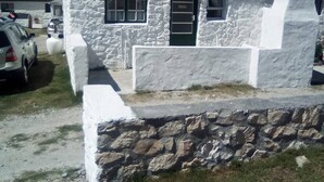 A white stone building with a flat roof, two windows, and a stone wall in front. - Quaint 1 Bedroom Apartment With sea View (Arniston)