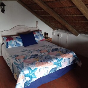 A bedroom with a bed, a nightstand, a lamp, and a sloped ceiling. - Quaint 1 Bedroom Apartment With sea View (Arniston)