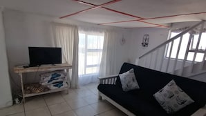 A living room with a sofa, a television on a stand, and a staircase. - Quaint 1 Bedroom Apartment With sea View (Arniston)