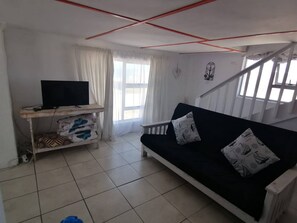 A living room with a sofa, a television on a stand, and a staircase. - Quaint 1 Bedroom Apartment With sea View (Arniston)