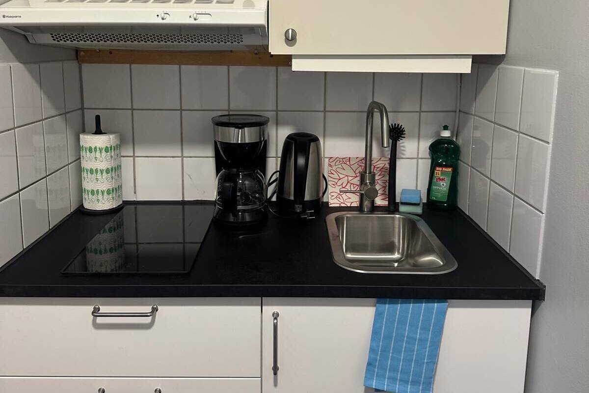 A kitchen with a black countertop, white cabinets, a stainless steel sink, a coffee maker, a kettle, and a dish soap bottle.