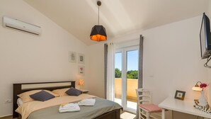 Quarto com cama, escrivaninha, cadeira, televisão e varanda.