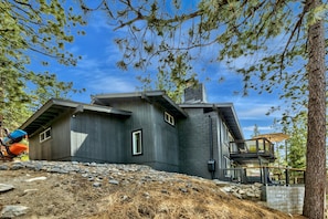 A modern house with a stone foundation, a wooden deck, and a large tree in the foreground. - Lake Views, Hot Tub Pool Table, Close To Heavenly! 3765o 4 Bedroom Home (South Lake Tahoe)