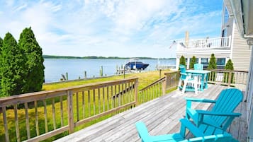 A wooden deck with outdoor seating, a view of a lake, and a dock with a boat.
