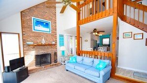Un salon avec une cheminée en briques, un canapé bleu, un téléviseur et un escalier en bois.