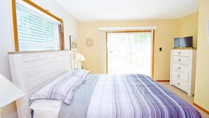 Une chambre à coucher avec un lit, une commode, un téléviseur et une fenêtre avec des stores.