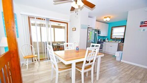 Un coin repas avec une table en bois et des chaises blanches, une cuisine avec des meubles de couleur turquoise et un ventilateur de plafond.