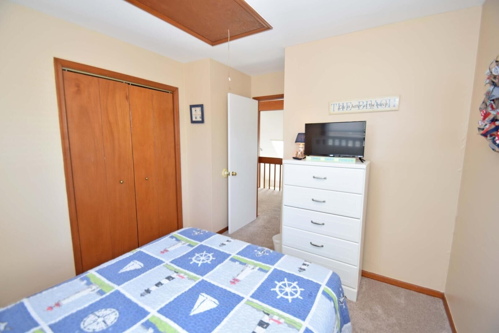Une chambre à coucher avec un lit, une commode, un téléviseur et une porte.