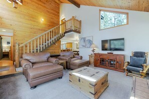 Ein geräumiger Wohnbereich mit einer Holztreppe, Ledersofas, einem Holztisch und einem Fernseher.