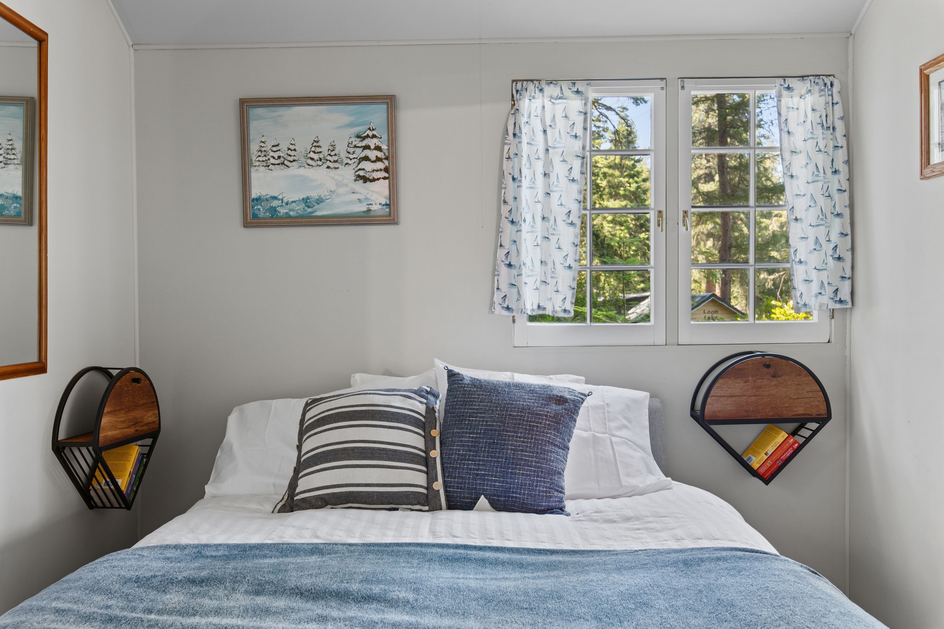 Une chambre à coucher avec un lit, deux étagères fixées au mur, une fenêtre avec des rideaux et un tableau accroché au mur.