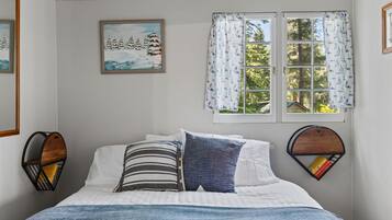 Une chambre à coucher avec un lit, deux étagères fixées au mur, une fenêtre avec des rideaux et un tableau accroché au mur.