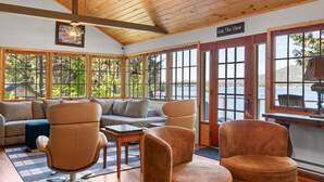 Una habitación amplia con techo de madera, ventanas grandes que ofrecen vistas al exterior, un sofá, dos sillones y una mesita.