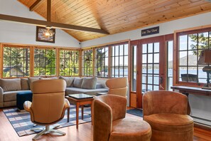 A spacious room with a wooden ceiling, large windows offering a view of the outdoors, a sofa, two chairs, and a small table. - Loon Lake Cabin w/ Private Beach & Dock (Loon Lake)