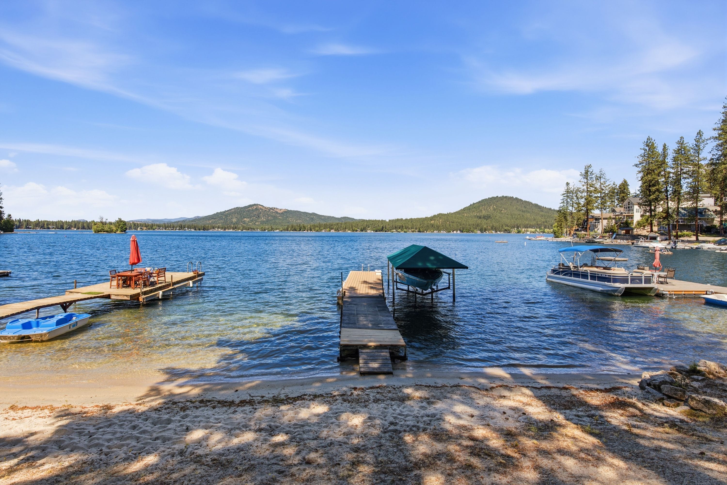 Une jetée au bord du lac avec des bateaux, une plateforme en bois, et une colline boisée en arrière-plan.