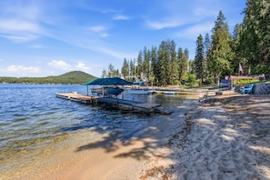 A lakeside beach with a dock, boats, and a small building with an American flag. - Loon Lake Cabin w/ Private Beach & Dock (Loon Lake)