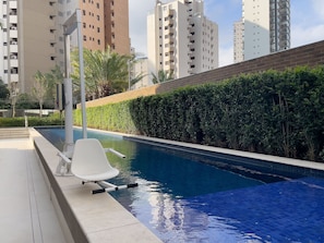 A swimming pool with a white lounge chair, surrounded by a brick wall and greenery, with tall buildings in the background. - 28m² 2 People Pool Gym (São Paulo)