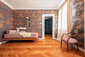 Ein Schlafzimmer mit Holzboden, einem Bett mit rosa Decke, einem Sessel und einem Spiegel an der Wand.