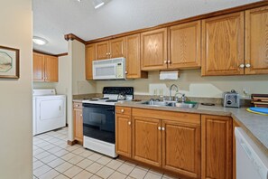 A kitchen with wooden cabinets, a microwave, a stove, a sink, and a toaster. - Coastal Escape Minutes from Cherry Grove! (North Myrtle Beach)